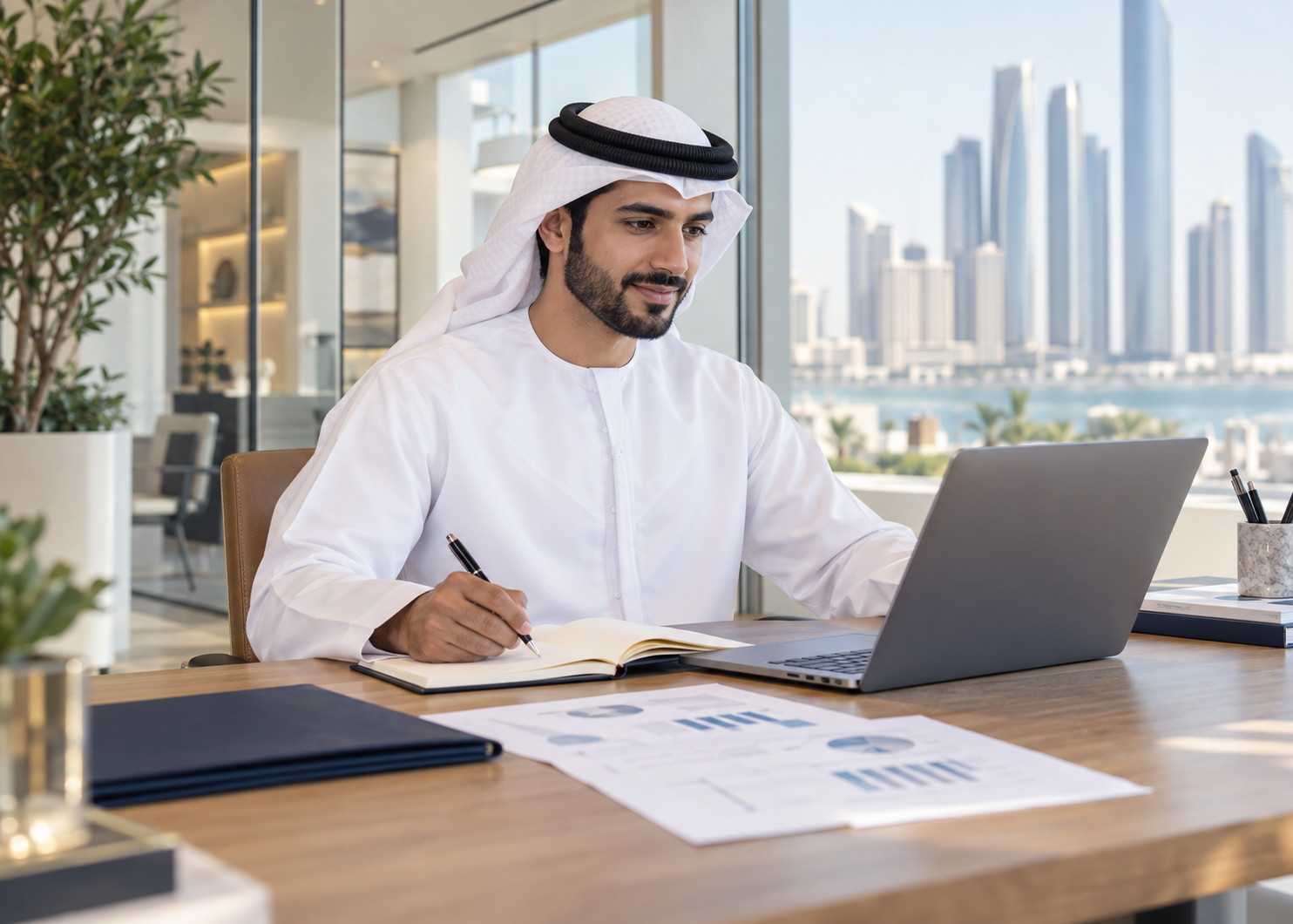 Emirati entrepreneur planning a new business using a laptop and notebook in an Abu Dhabi office.